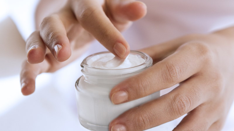 Zoom sur un pot de crème hydratante, tenu dans des mains.